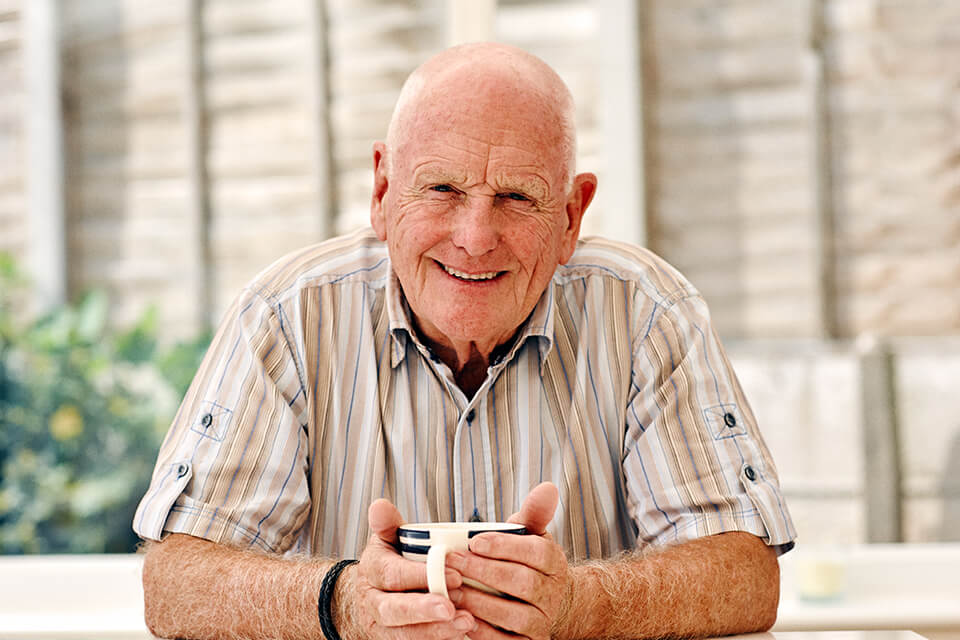 An older man holding a mug and smiling